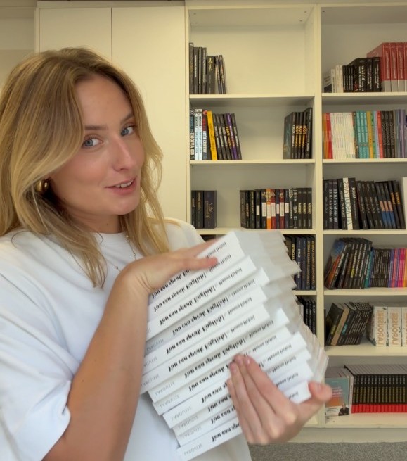 photo de l'autrice avec une pile de ses livres dédicacés